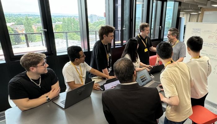 Nine people smiling and having a discussion in front of a whiteboard.