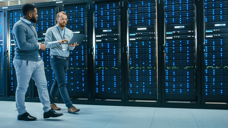 Two engineers walking through a server room filled with racks of glowing blue lights.