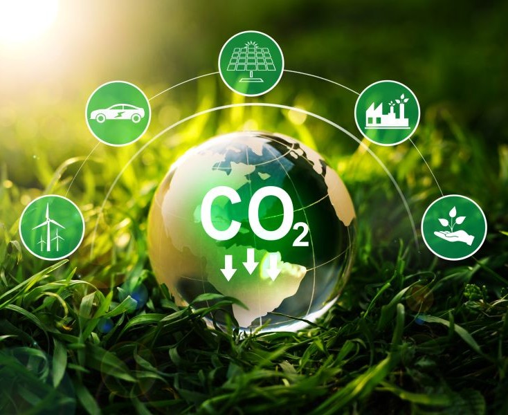 Globe showing CO₂ reduction surrounded by low-carbon icons, on grass with sunlight